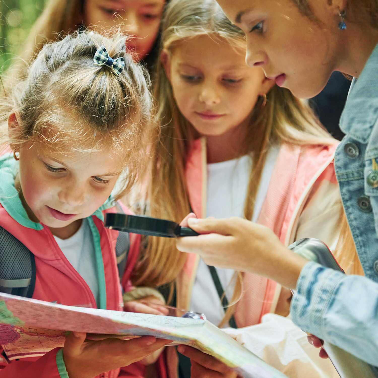 A group of school aged kids gather around a map with a magnify glass.