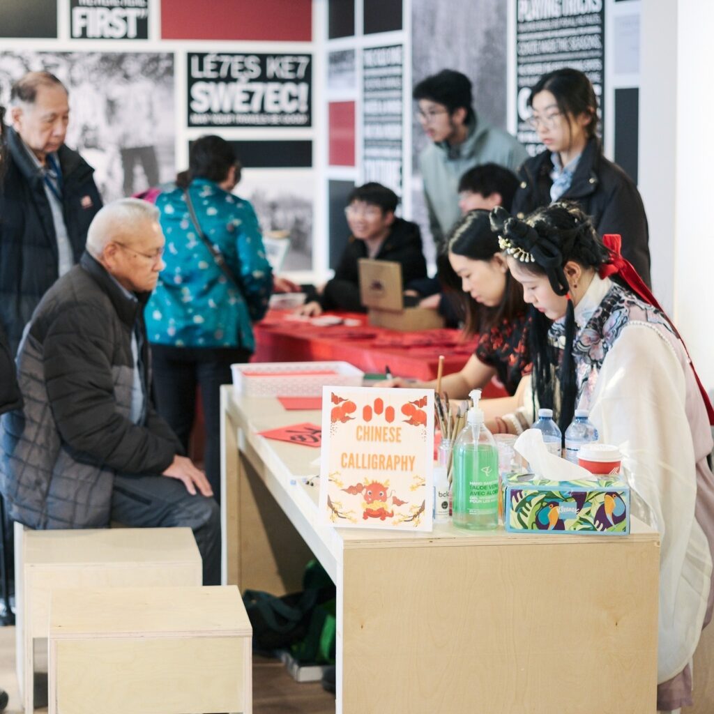 Volunteers sit at a table with guests drawing ink symbols.