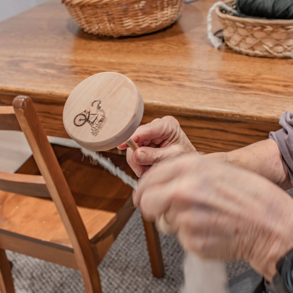 A wooden hand spinner, often called a drop spindle, uses gravity to spin wool fibres into yarn. By gently twisting the fibres while the spindle spins downward, this traditional tool allows crafters to create fine, even yarn with skillful hands and simple mechanics.